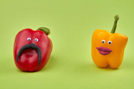 Bell peppers with faces. Male and female ripe colored bell peppers isolated on light green background.の写真素材