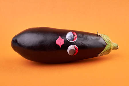 Eggplant with sexy female face. Lying black plant isolated on orange background.の写真素材