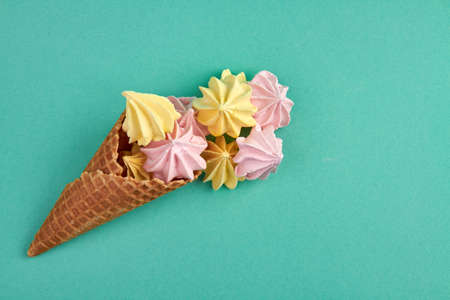 Ice-cream cone with colored zephyrs candies. Sweet dessert isolated on turquoise background.