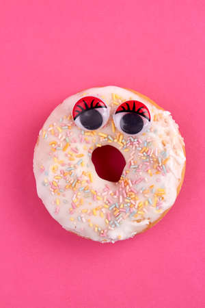 Female donut with funny eyes. Sweet donut with sprinkle candies isolated on pink background.の写真素材