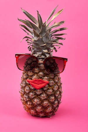 Female exotic fruit concept. Pineapple with glasses and red lips isolated on pink background.
