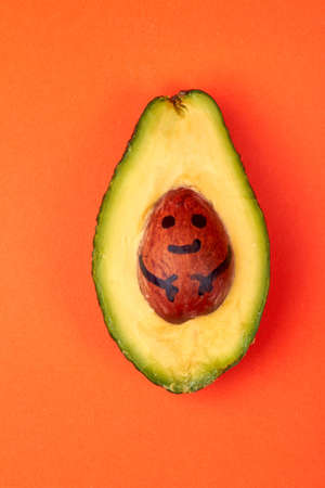 Avocado newborn concept. Half avocado with seed symbolizing baby. Isolated on orange background.