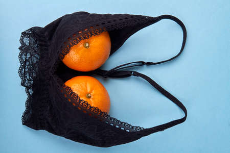 Two ripe mandaring into bra. Small female breast concept. Isolated on blue background.の写真素材