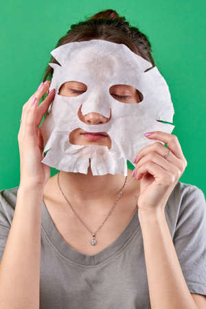 Portrait of girl applying paper spa mask. Using health skin mask isolated on green background.の写真素材