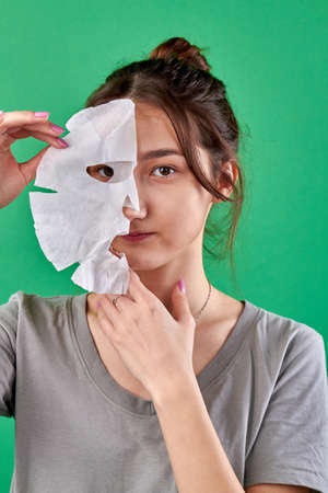 Womans holding half of a paper spa mask. Isolated on green chromakey background.の写真素材