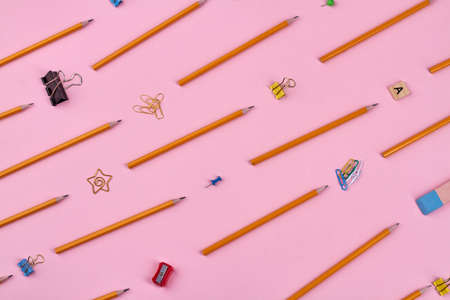 School accessories for studying. Pencils, sharpeners and paper clips on pink background.