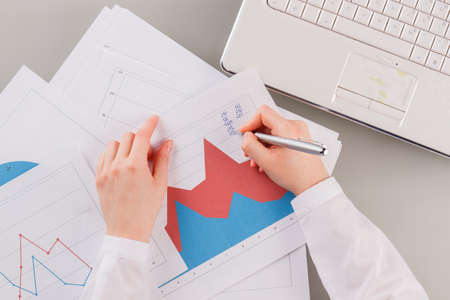 Female hand writing on business documents. Close up of business woman hands writing on graphs and...