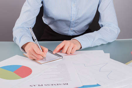 Close up business woman writing on notepad with a pen. Female accountant analyzing charts and graphs showing results.の写真素材