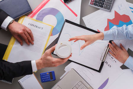 Businessman giving coffee to woman over table with documents. Business partners analyzing financial...