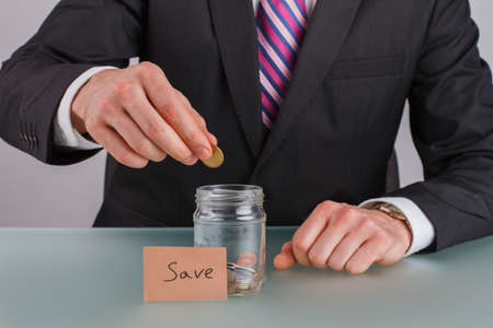 Male hand putting coins into glass jar for saving money. Savings and investment concept.の写真素材