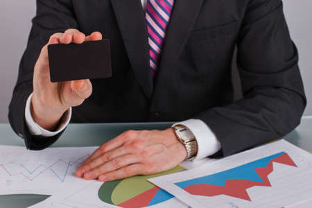 Businessman showing business card while sitting at table. Financial expert analyzing business documents.の写真素材
