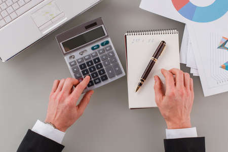 Male accountant working with financial data at office. Business man using calculator and paper...