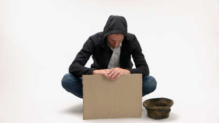 Poor sad man with blank cardboard sign. Young guy begging with donation hat isolated on white...