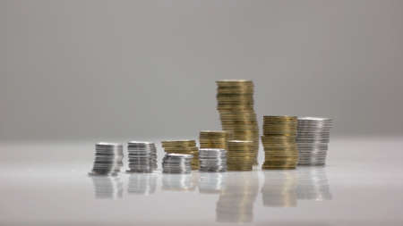 Stacks of coins on white reflective surface. Columns of silver and golden coins.