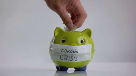 Hand puts glove into piggy bank. Donation for coronavirus pandemic.の写真素材