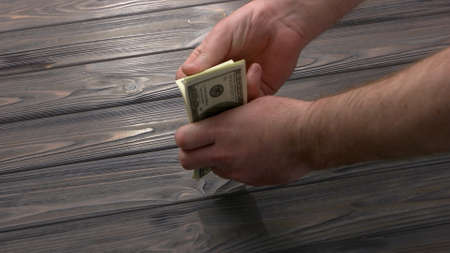 Close-up mans counting his money. Male hands with bunch of dollars. Rustic wooden table.の写真素材