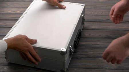 Close-up man with silver metal briefcase. Mans giving a big bribe. Dark wooden table surface.