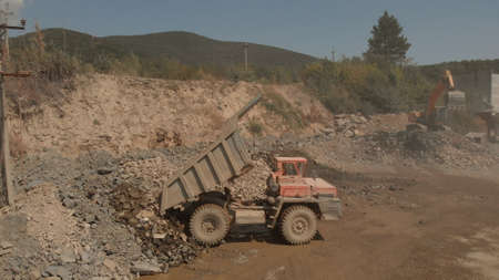 Dump with stones and sand. Digger machine is picking up stones on the background.の写真素材