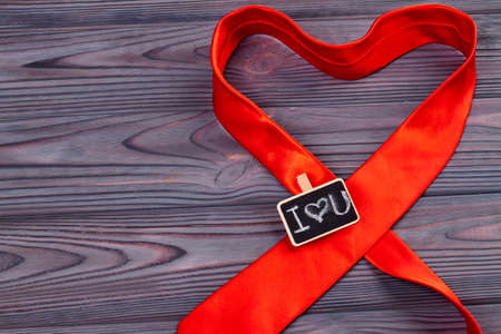 Red tie as a symbol of love. Shape of heart. Dark wooden desk.の写真素材