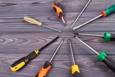 Varoius screwdrivers arranged in a circle. Grey wooden background.