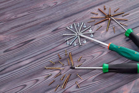 Three screwdrivers surrounded with screws. Grey wooden desk.の写真素材