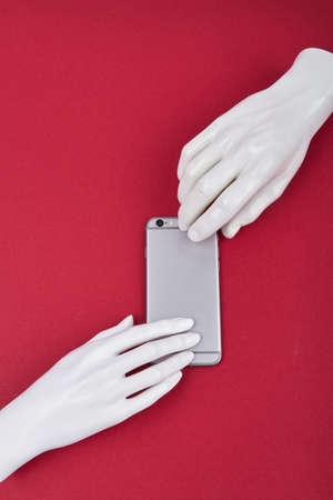 Vertical shot mannequins hands and smartphone. Isolated on red background.