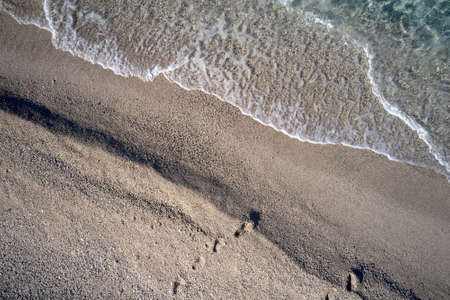 Background of soft wave sea foam and sandy beach. Sea waves reaching shore. View from above.