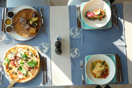 Top view of restaurant table with food. Tasty appetizers, salads and pizza. Different meals for the...