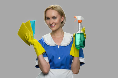 Young smiling cleaner woman. Young pretty woman maid in uniform holding rags and bottle of cleaning spray. Cleaning concept.の写真素材