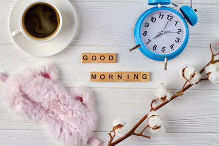 Good morning composition top view. Alarm clock spring willow sleep mask and empty coffee cup on white wood.の写真素材