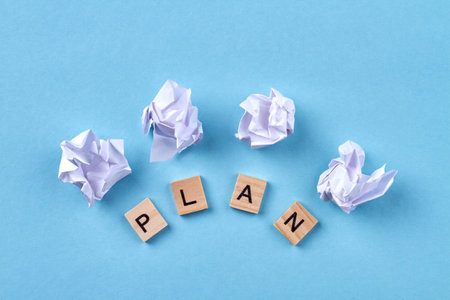 Plan word made with building blocks. White balls of paper isolated on blue background.