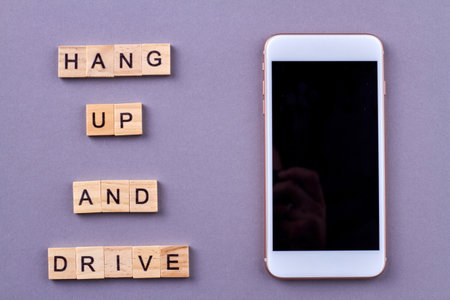 Slogan for safety on the road. Phrase hang up and drive. White smartphone near wooden letter cubes. Isolated on purple background.の写真素材