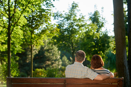 Mature couple on the bench. back view senior wife and husband in the green summer park.の写真素材