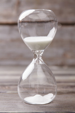Close-up hourglass with white sand. Vertical shot old wood background.