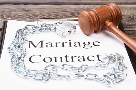 Concept of marriage as a prison. Marriage contract with metal chains and wooden gavel.の写真素材