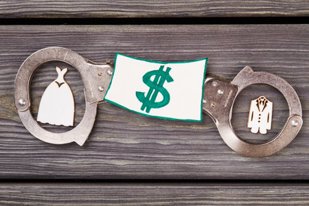 Family crime law concept. Handcuffs with miniature custumes and money on wood.の写真素材