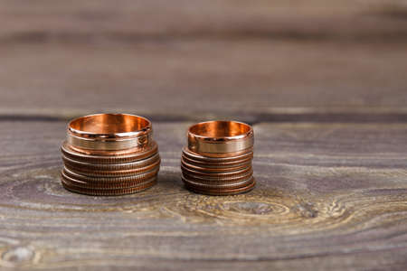 Stacks of coins and golden rings. Brown wooden background.
