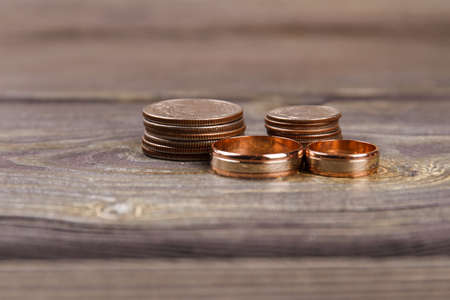 Close-up golden coins and wedding rings. Wooden table background.の写真素材
