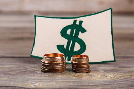Dollar sign and stacks of coins. Two wedding rings. Wooden desk background.
