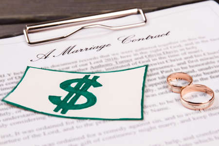 Dollar sign and wedding rings. Close-up marriage contract on the clipboard.の写真素材