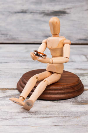 Miniature wooden mannequin with wedding ring. Sitting dummy holding golden ring vertical shot.の写真素材