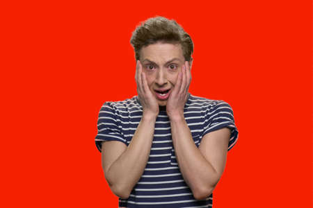 Crying teen boy touching his face with both hands. Isolated on red background.