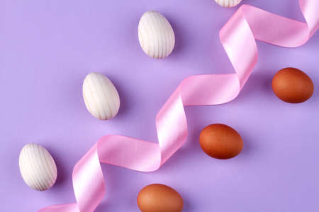 Boiled chicken eggs and swirled pink tape isolated on purple background.