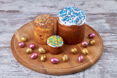 Easter eggs and cakes on round wooden board.