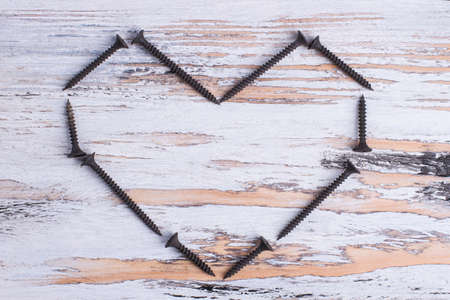 Heart shape from black screws on wooden background.