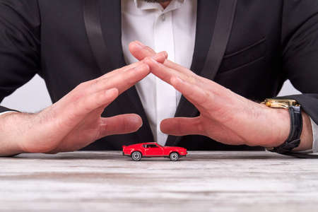 Close-up businessmans hands protecting a toy car model.の写真素材