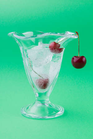 Vertical shot of ice-cream glass cup with ice and cherries.