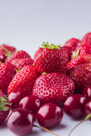 Vertical shot close-up pile of red cherries and strawberries.