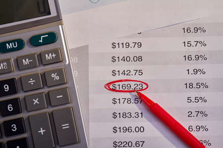 Calculator with red pen and bills with outlined number.