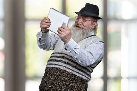 Funny senior man using digital tablet and looking surprised.